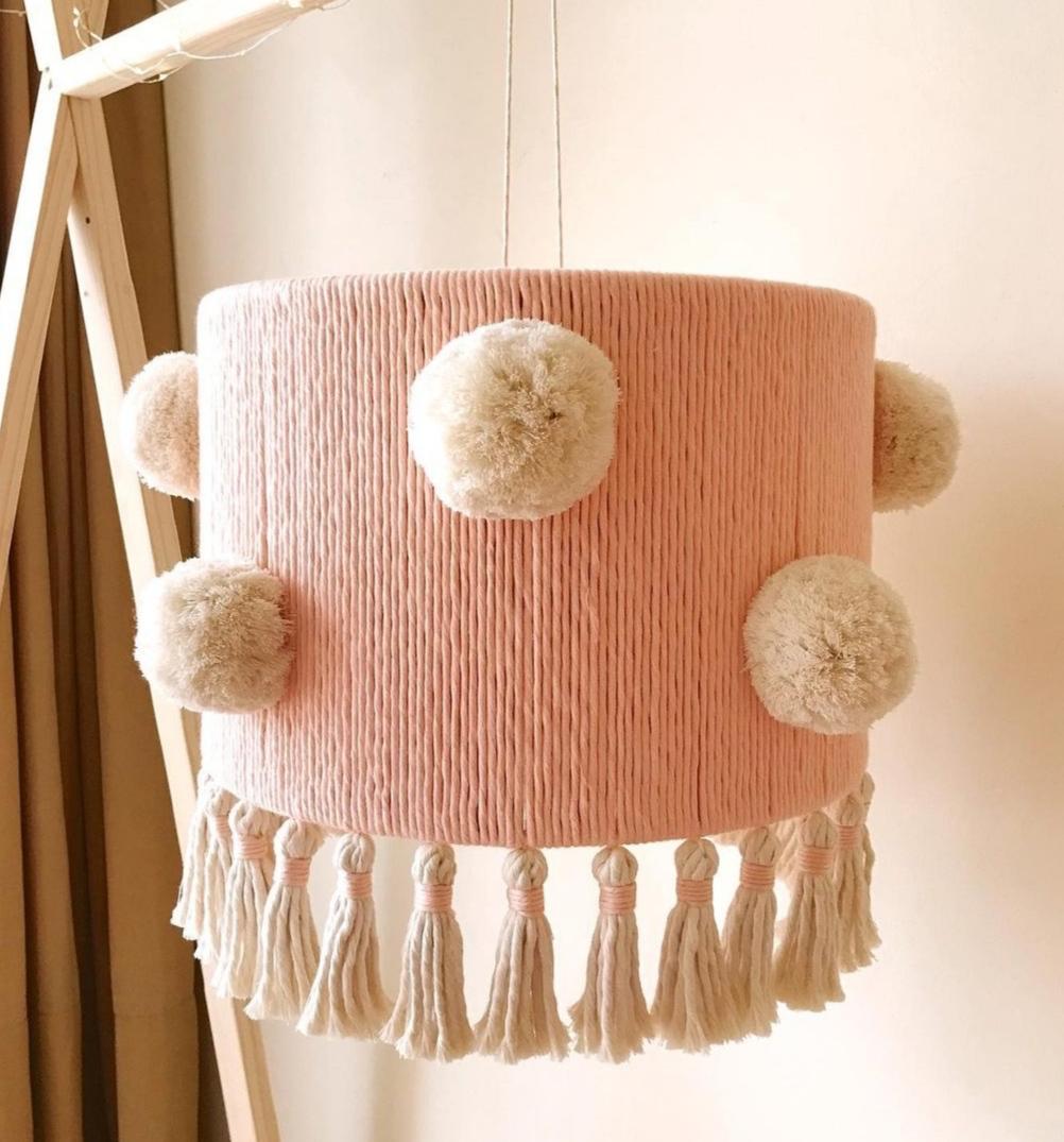A soft, handmade nursery lampshade featuring delicate cotton tassels and fluffy pompoms. This cozy, bohemian pink chandelier brings a warm, soft light to any room. Perfect for a nursery or a modern, minimalist interior.